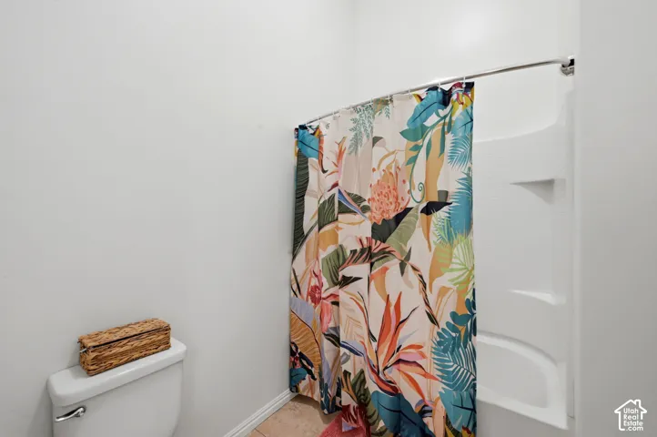 Bathroom featuring a white toilet, light-toned tile flooring, and a white shower/tub combination with integrated shelving