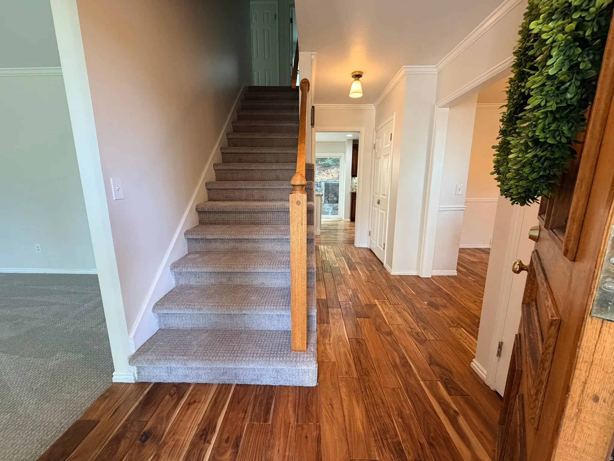 Entryway featuring rich wood-finish flooring, a carpeted staircase with a wood handrail, white trim, and a decorative light fixture
