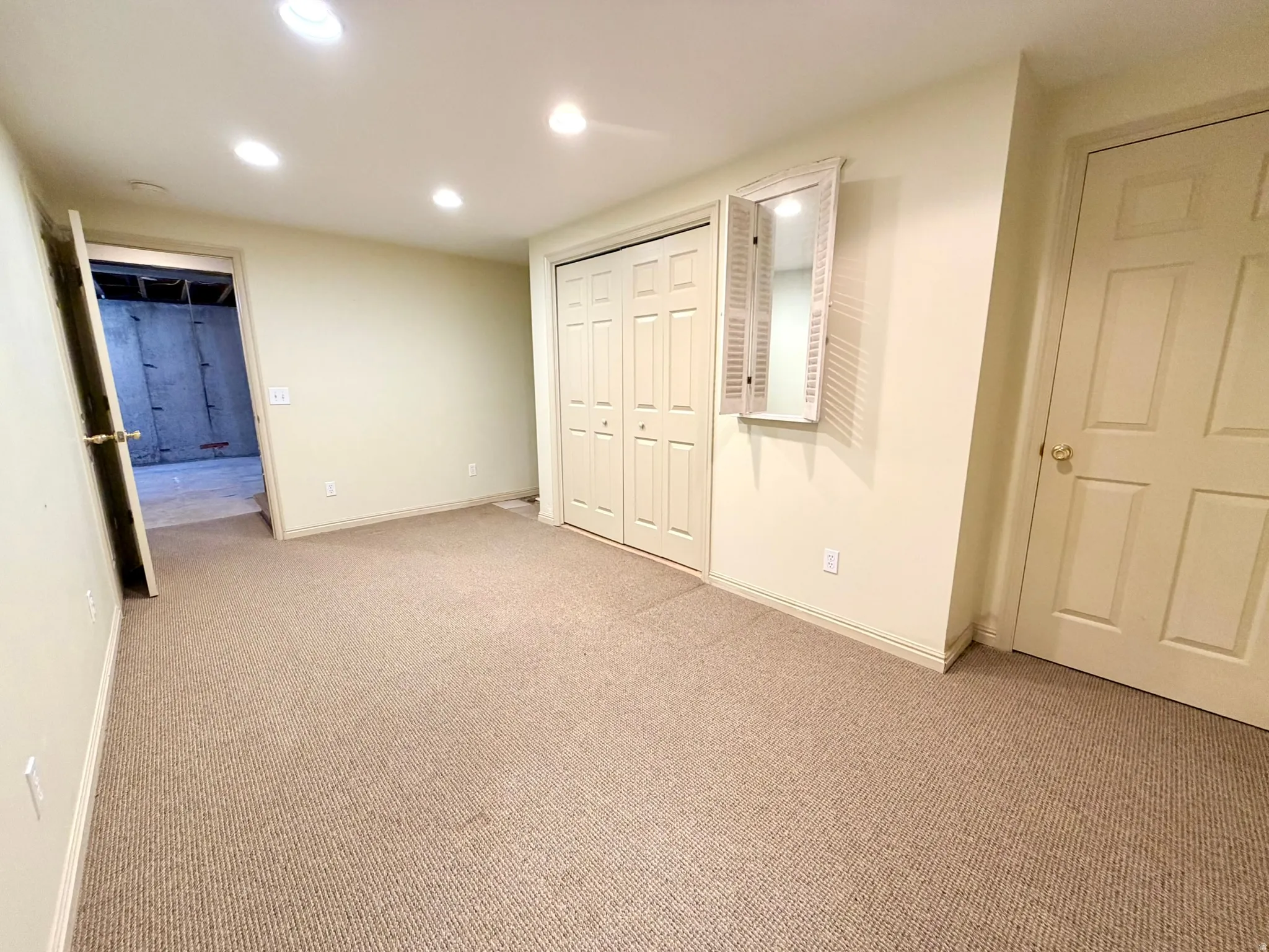 Carpeted room featuring recessed lighting, a bifold door closet, an interior door with brass hardware, and a decorative wall mirror with shutter details