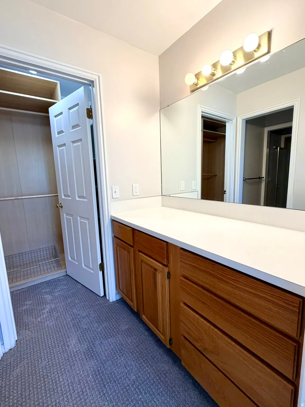 Vanity area featuring a wood-finish cabinet with multiple drawers and doors, a white countertop, and a full-width mirror with a four-bulb vanity light fixture in Primary bathroom