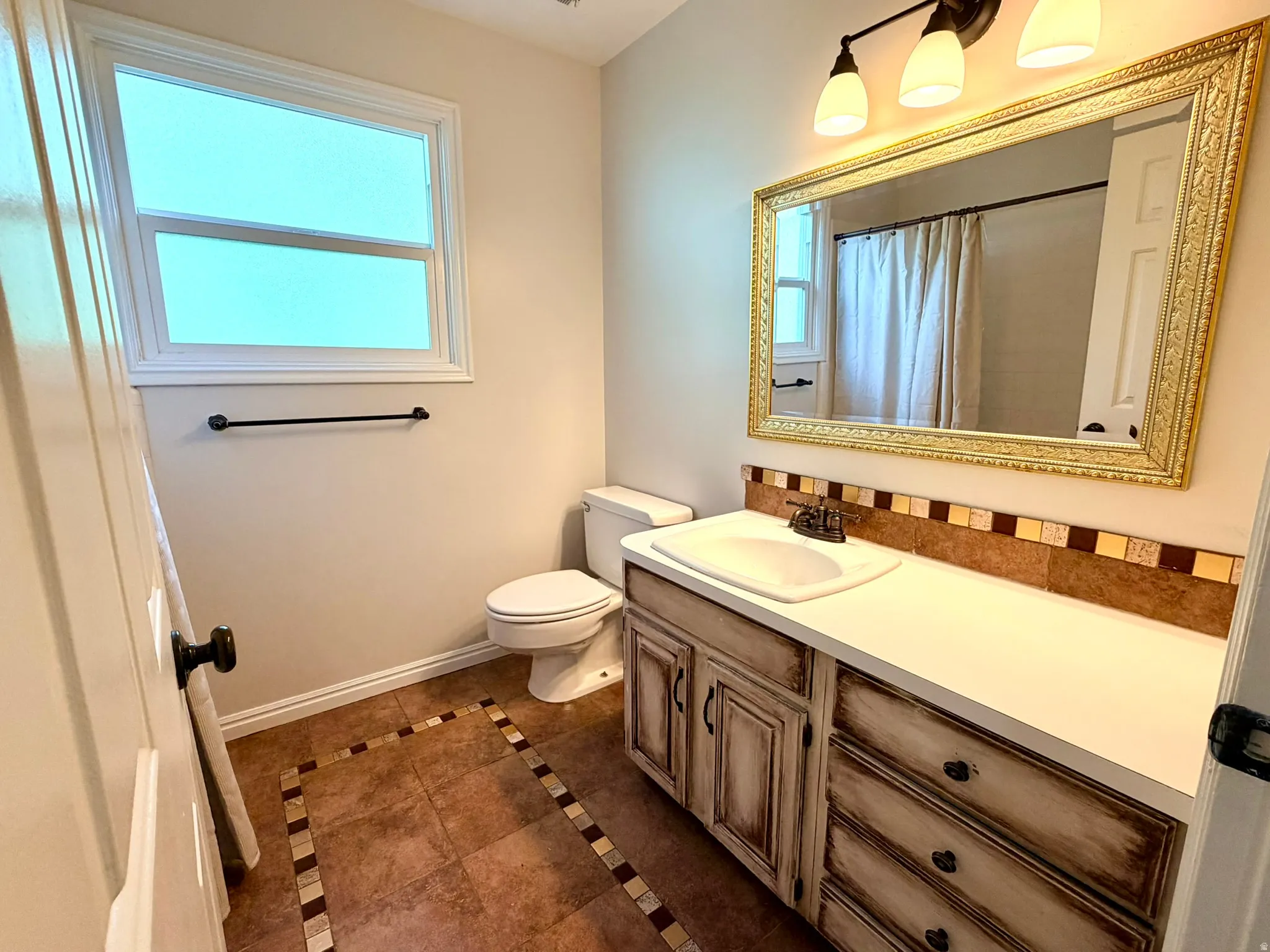 Bathroom featuring a distressed wood-finish vanity with an integrated sink, a large ornate gold-framed mirror, and a three-light vanity fixture