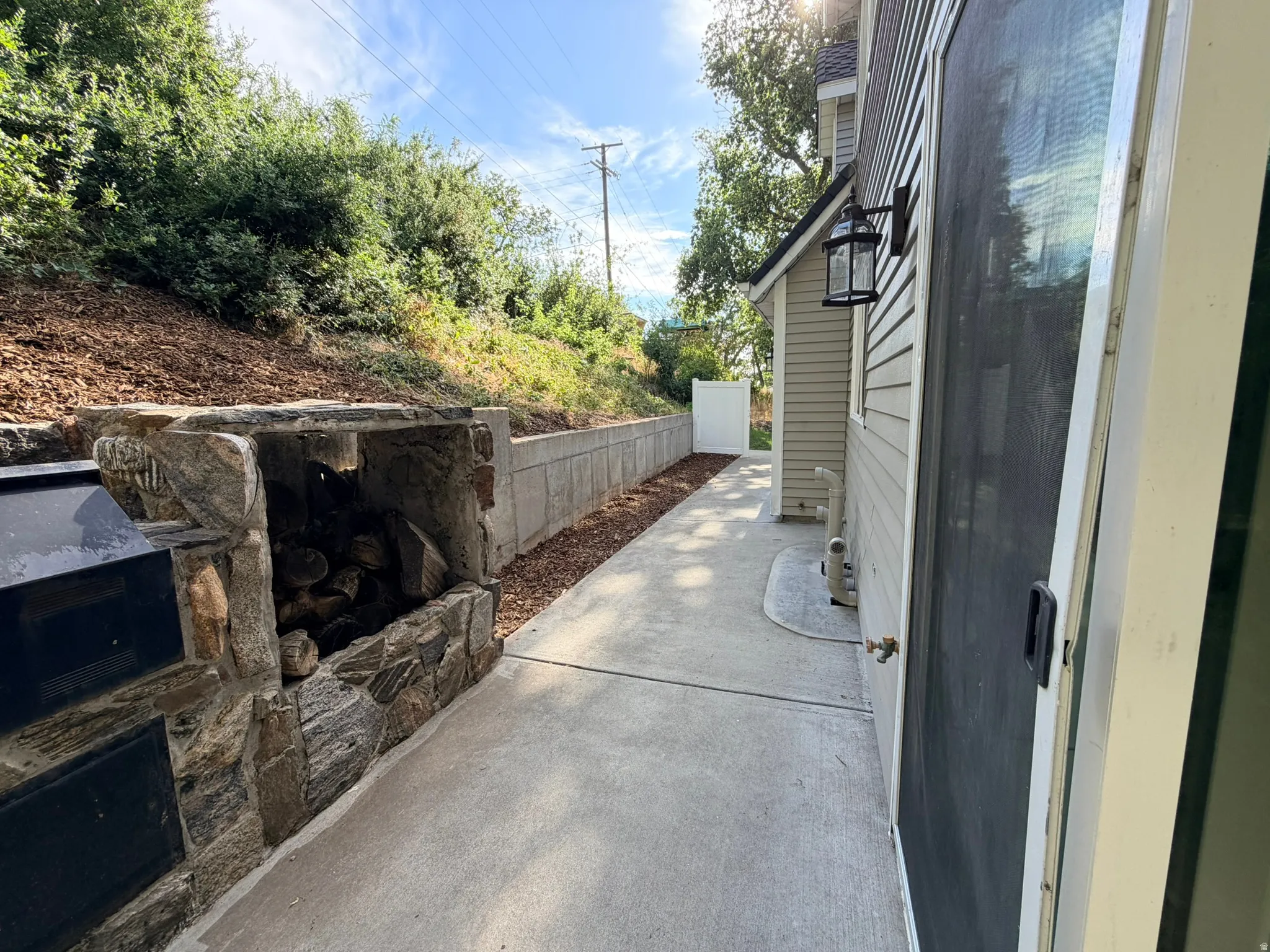 Concrete pathway featuring a stone-clad outdoor fireplace with log storage