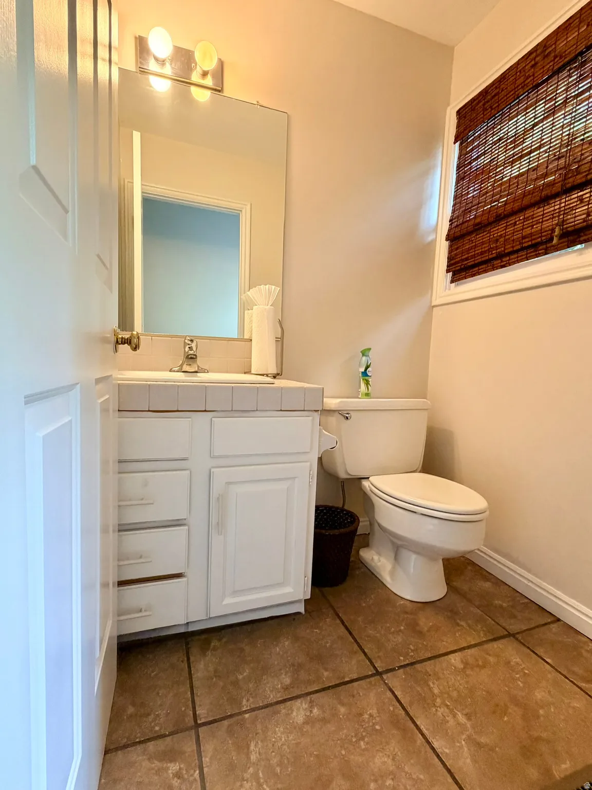 Ceramic tile flooring, white vanity with integrated sink, rectangular mirror, and wall-mounted lighting fixture