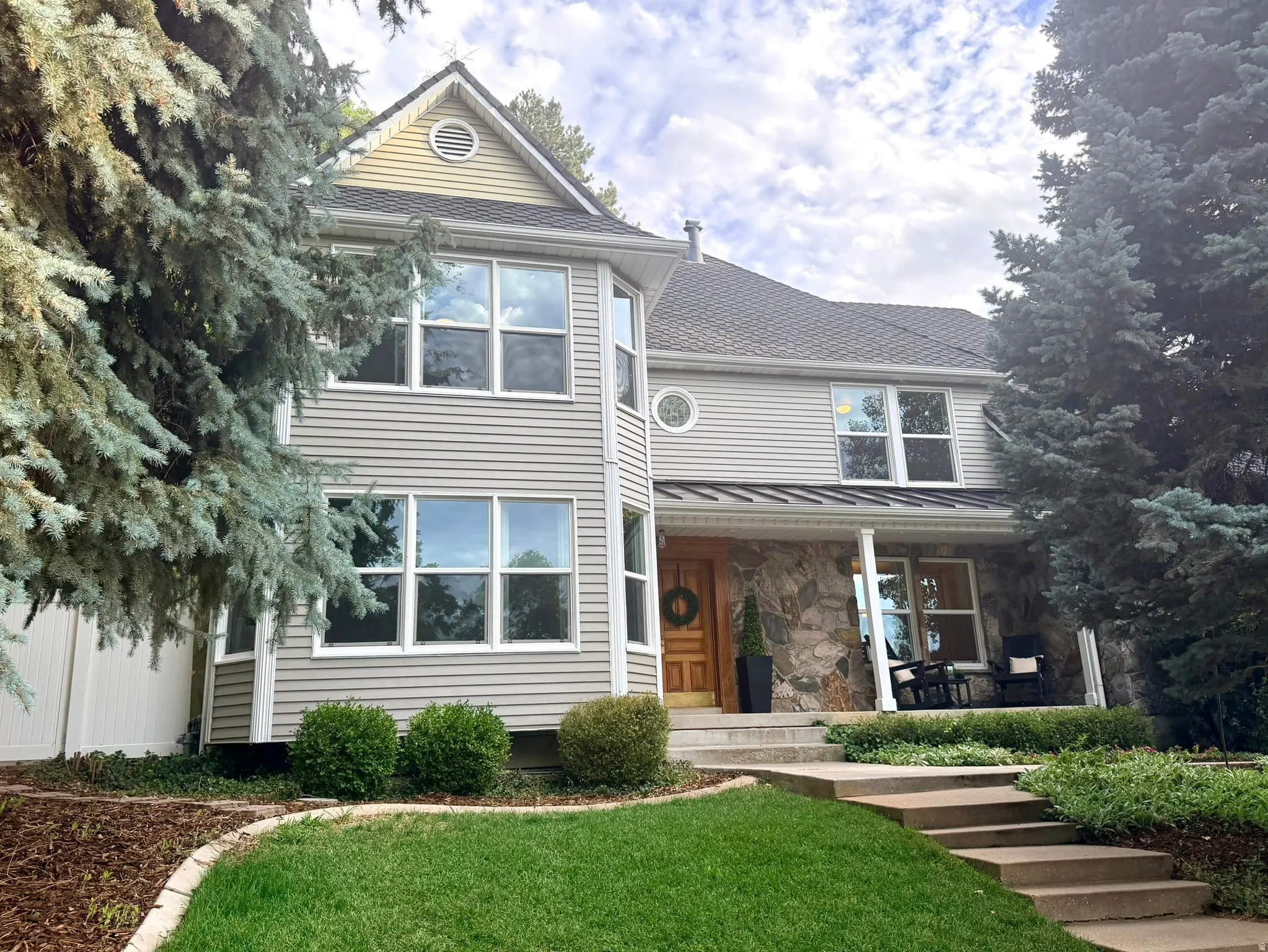 Two-story residence featuring siding and stone facade, a covered entry porch, and mature trees