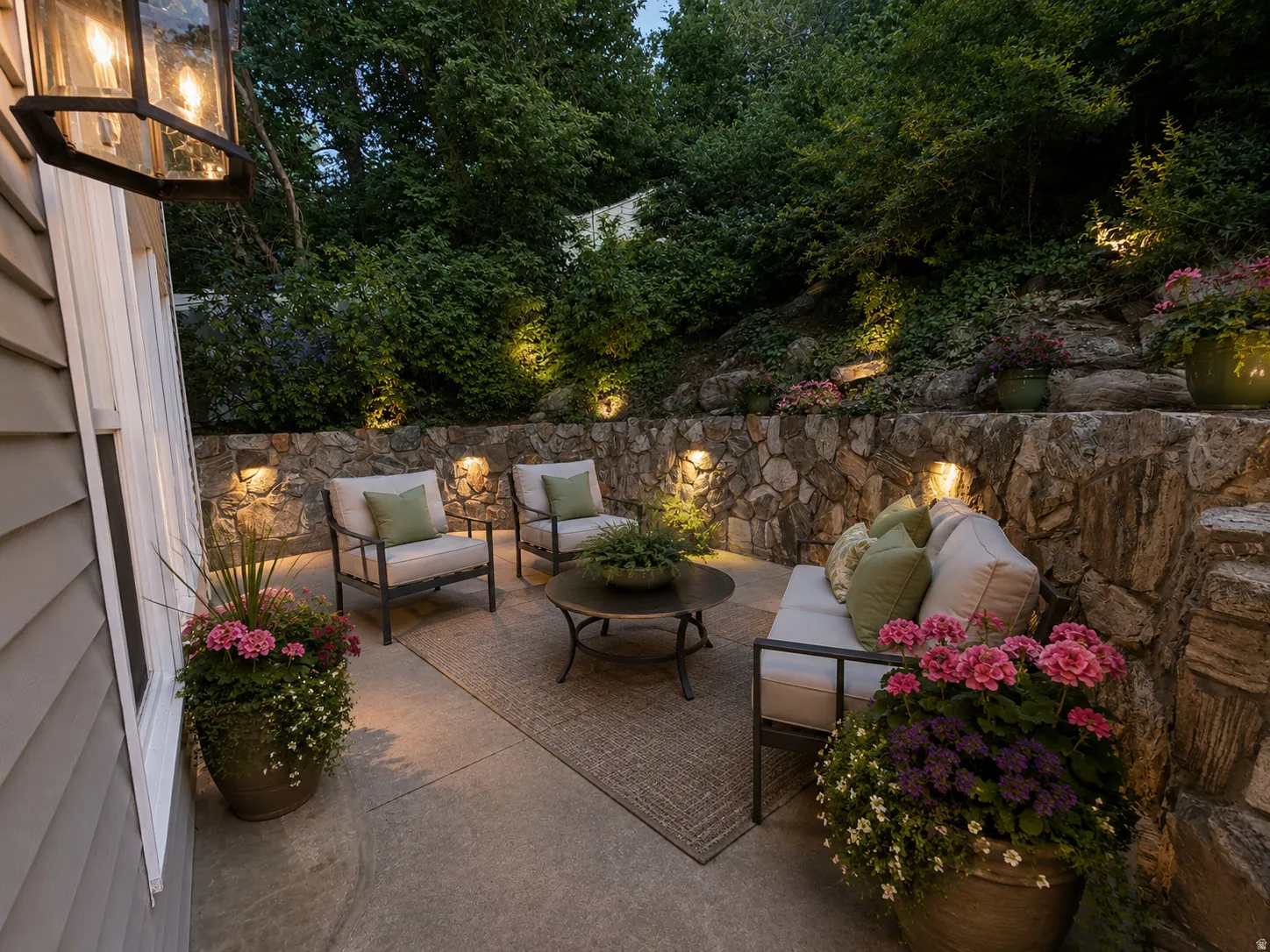 Patio area with concrete hardscaping, stone retaining walls, and integrated landscape lighting