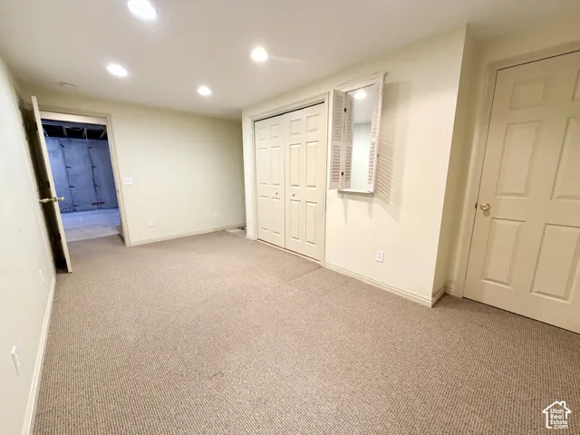 Carpeted room featuring recessed lighting, a bifold door closet, an interior door with brass hardware, and a decorative wall mirror with shutter details