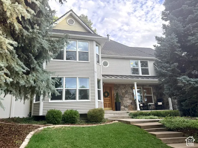 Two-story residence featuring siding and stone facade, a covered entry porch, and mature trees
