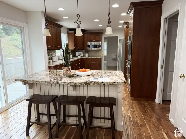 Kitchen featuring a center island with a speckled countertop, brown wood-finish cabinetry, stainless steel double wall oven, recessed lighting, and wood-finish flooring