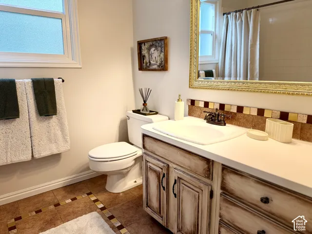 Bathroom featuring a white vanity top, distressed wood-finish vanity, tiled backsplash, and decorative floor tiling