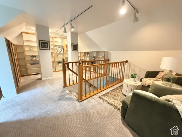 Built-in shelving, natural wood staircase railing, track lighting, and sloped ceilings