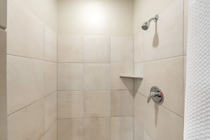 Shower enclosure featuring light-toned tile walls and a chrome showerhead
