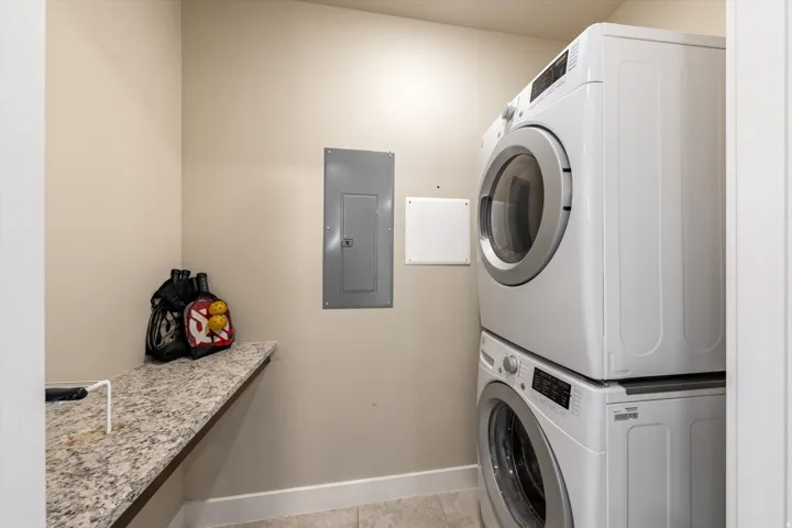 Dedicated laundry area featuring a stacked washer and dryer, a granite-look countertop, and neutral wall paint