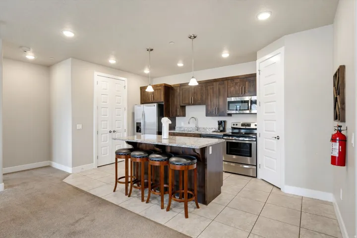 Modern kitchen featuring a central island with a granite countertop, dark wood cabinetry, stainless steel appliances, and recessed lighting