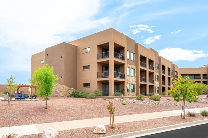 Multi-story stucco exterior featuring individual balconies with black railings, stone veneer accents, and a paved walkway