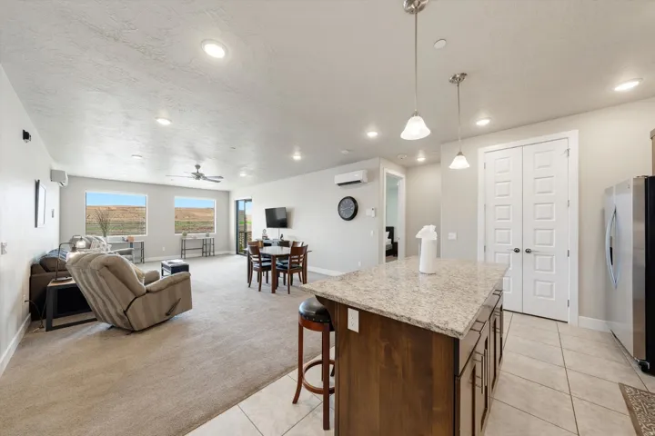 Spacious open-concept living area featuring a kitchen island with stone countertop, wood-finish cabinetry, recessed lighting, and large windows