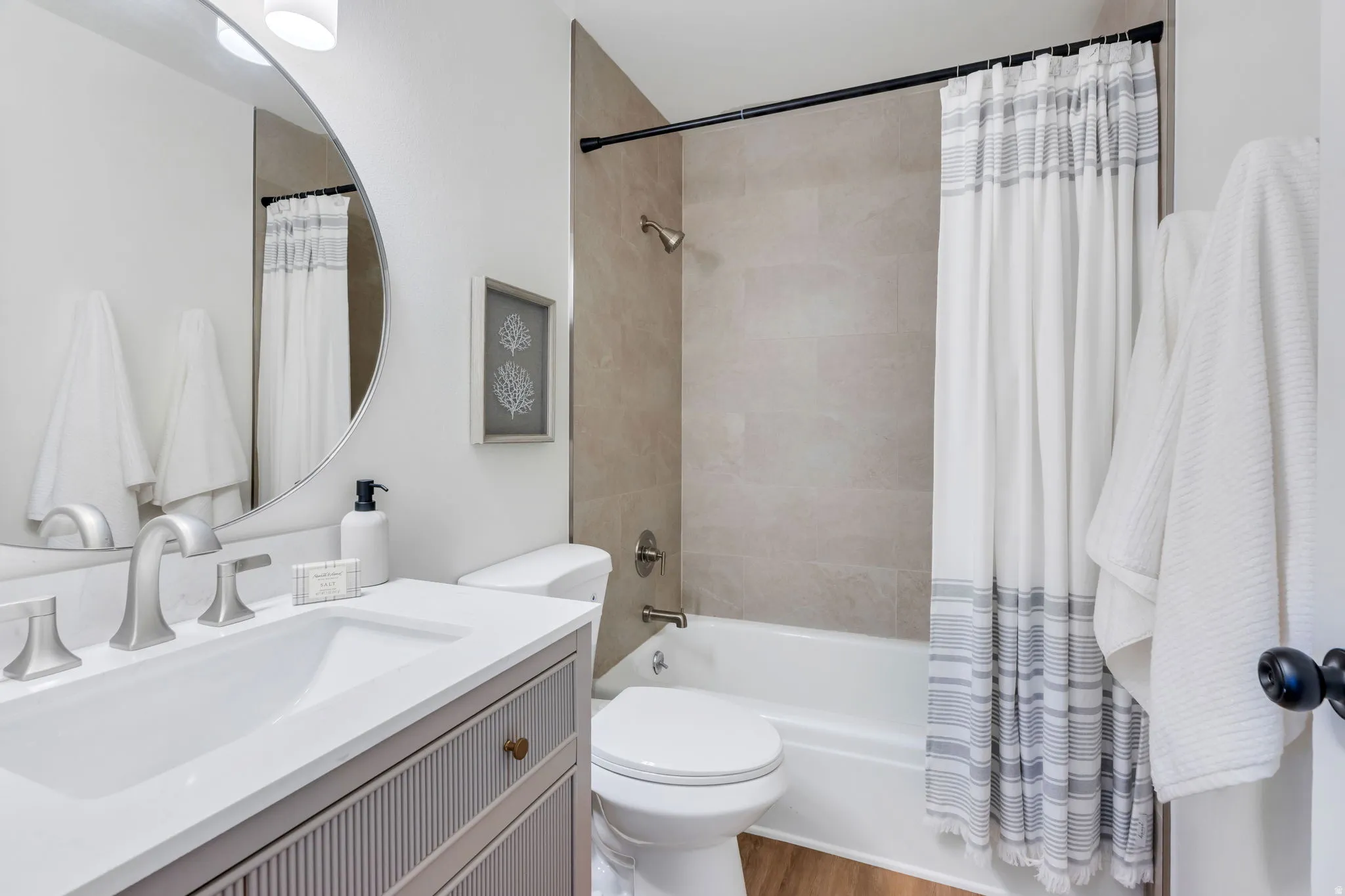 Bathroom featuring a modern vanity with integrated sink, brushed nickel fixtures, a round mirror, and a full-size bathtub with tiled surround