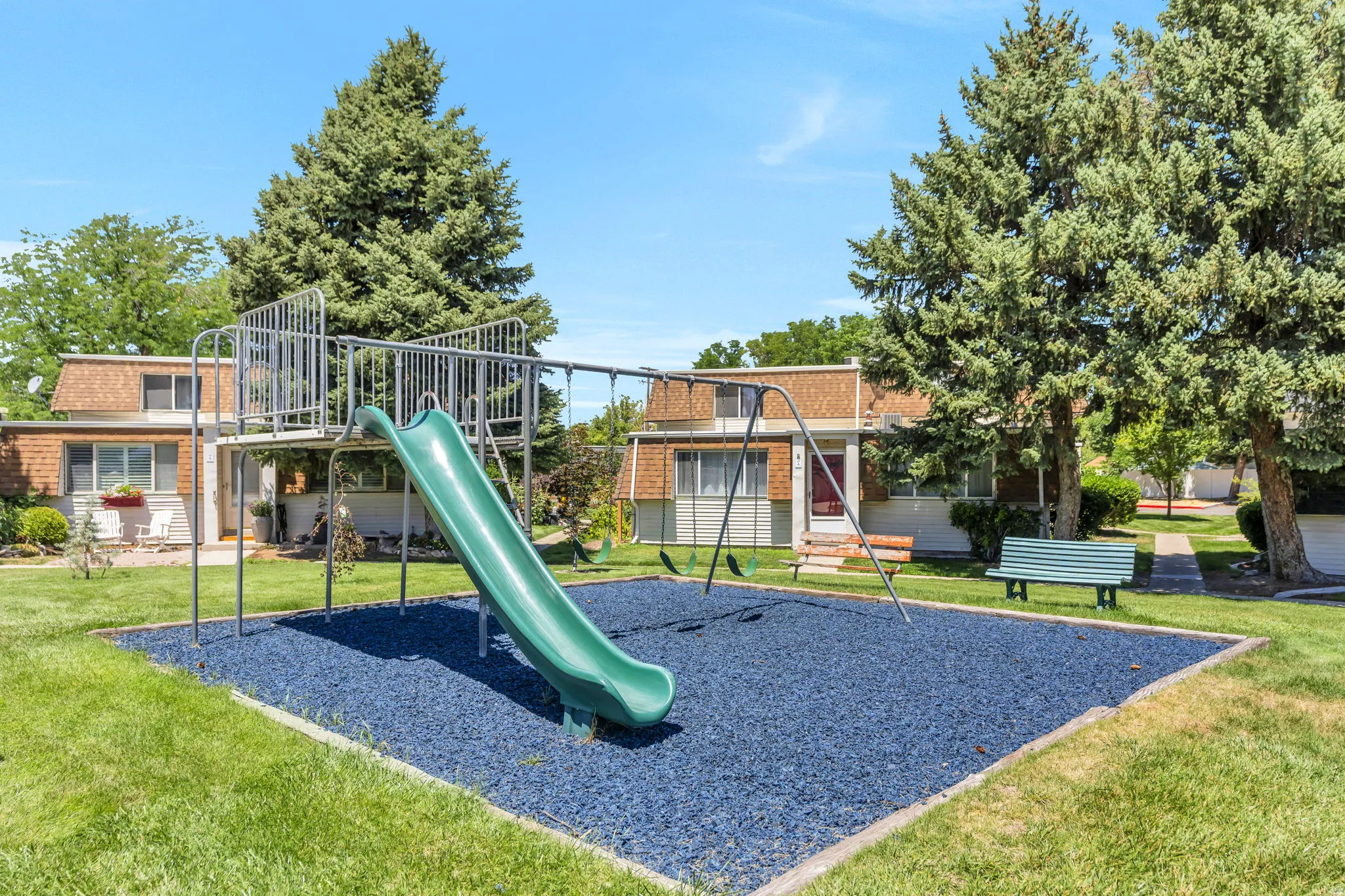 Community playground featuring a slide, swing set, and blue rubberized safety surfacing