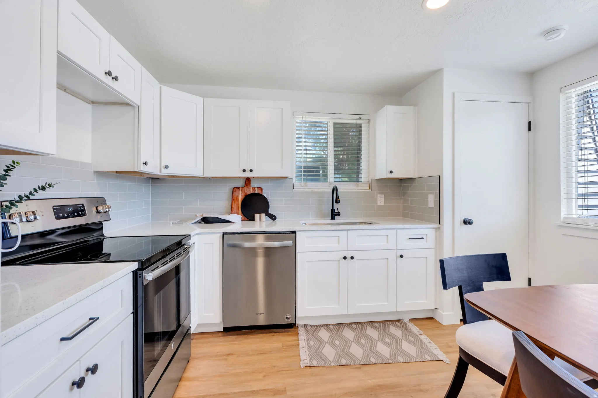 Modern kitchen featuring white shaker cabinetry with black hardware, light-toned countertops, and a subway tile backsplash