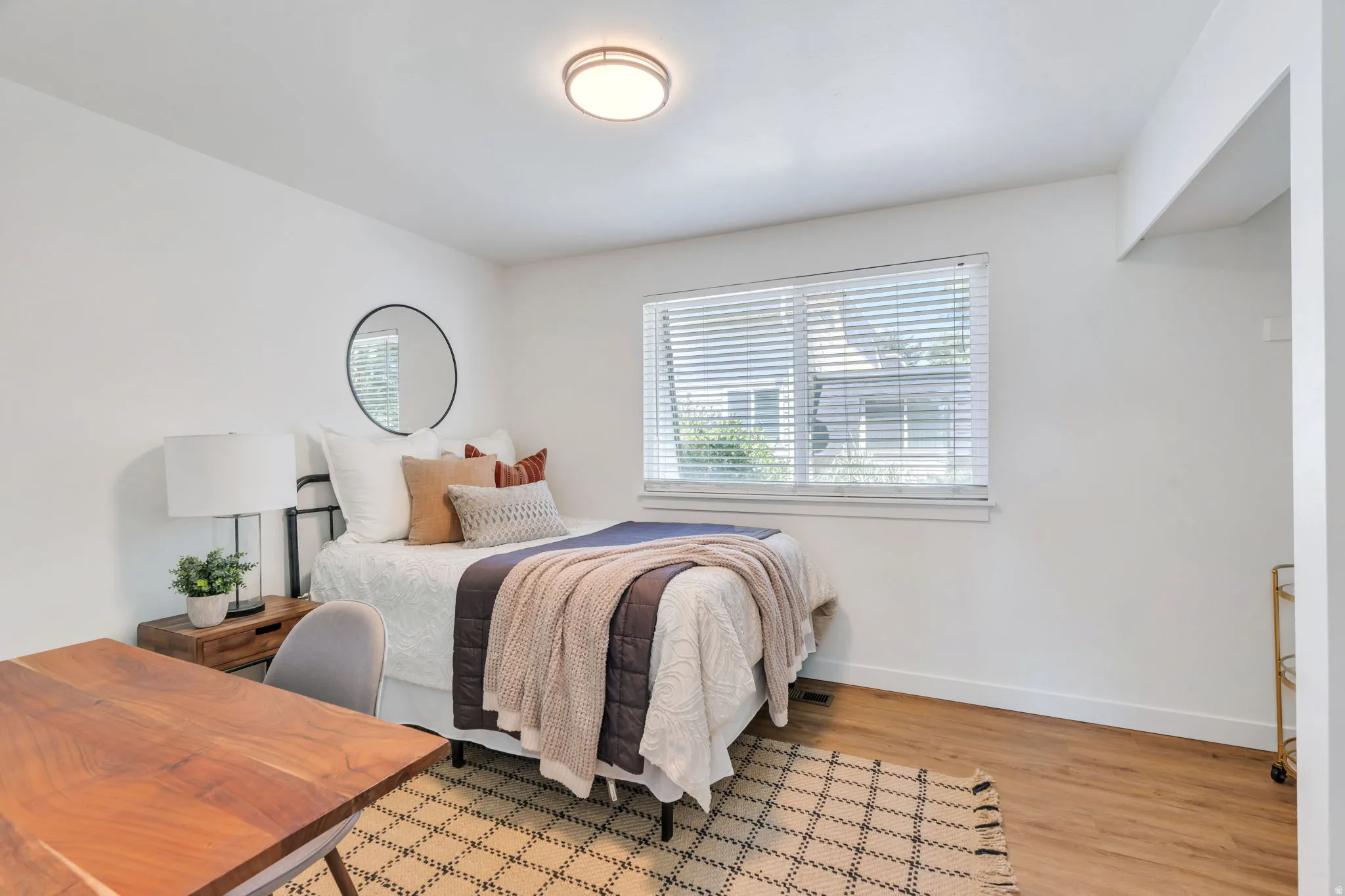Bedroom with wood-finish flooring, a window featuring blinds, and white baseboards