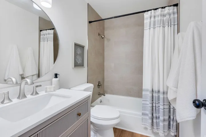 Bathroom featuring a modern vanity with integrated sink, brushed nickel fixtures, a round mirror, and a full-size bathtub with tiled surround