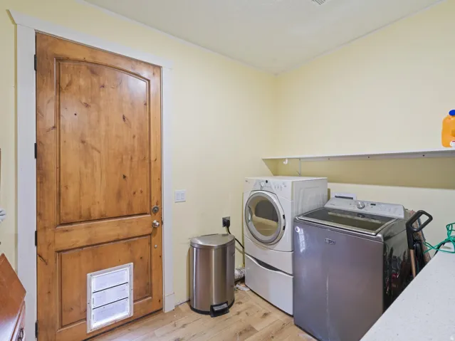 Laundry area featuring a wood-finish door with white trim, light-toned walls, and wood-finish flooring