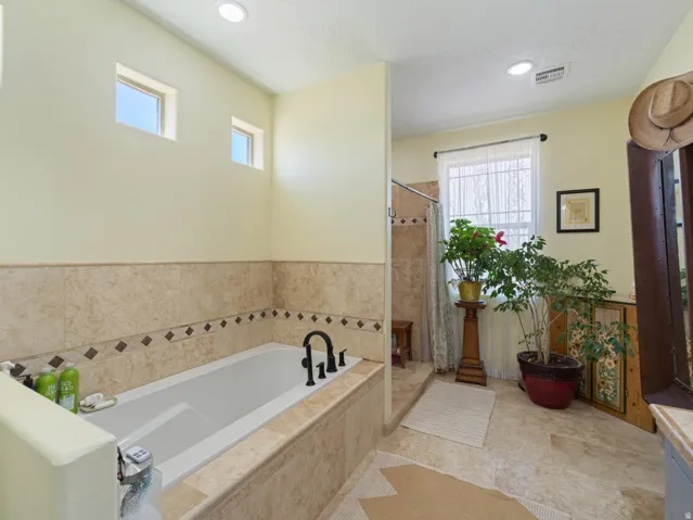Soaking tub with a black faucet, surrounded by natural stone-look tile with decorative accents