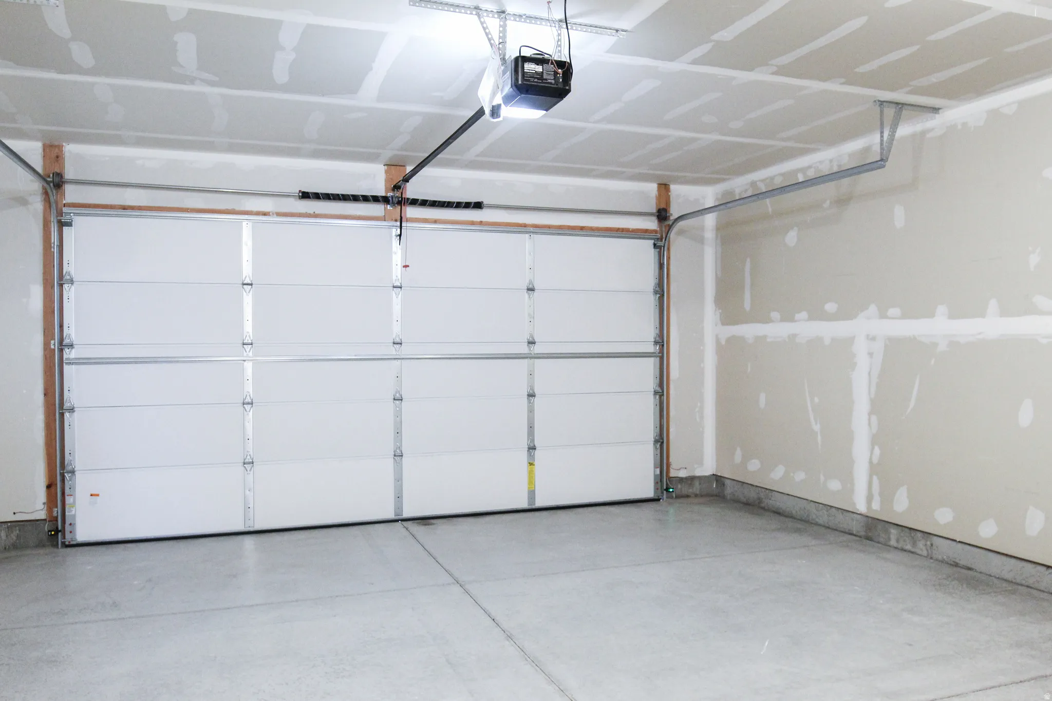 Spacious garage featuring a concrete floor, an overhead garage door, an automatic opener, and unfinished drywall