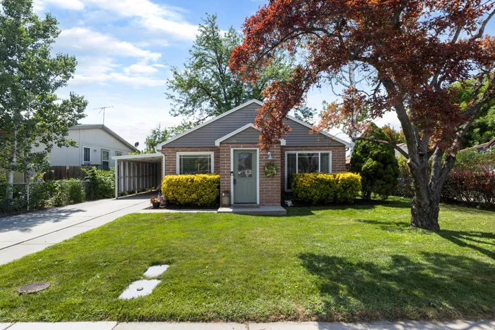 Brick exterior with gray siding accents, featuring a covered carport and a verdant front lawn