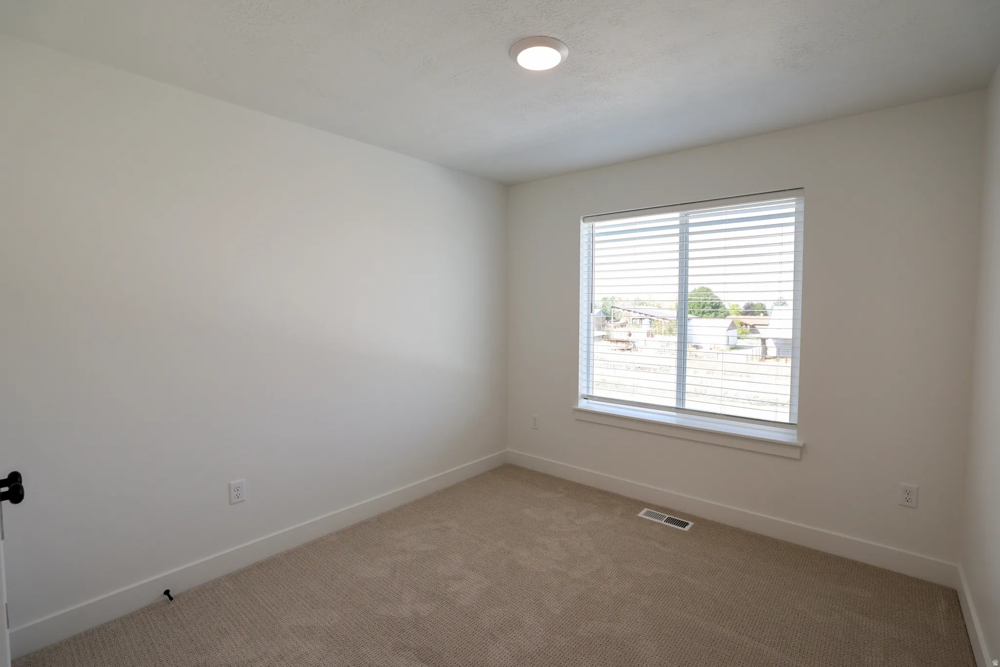 Neutral tone walls and carpeting, featuring a window with horizontal blinds