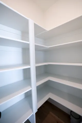 Spacious walk-in pantry featuring multiple levels of built-in shelving, white finishes, and wood-finish flooring