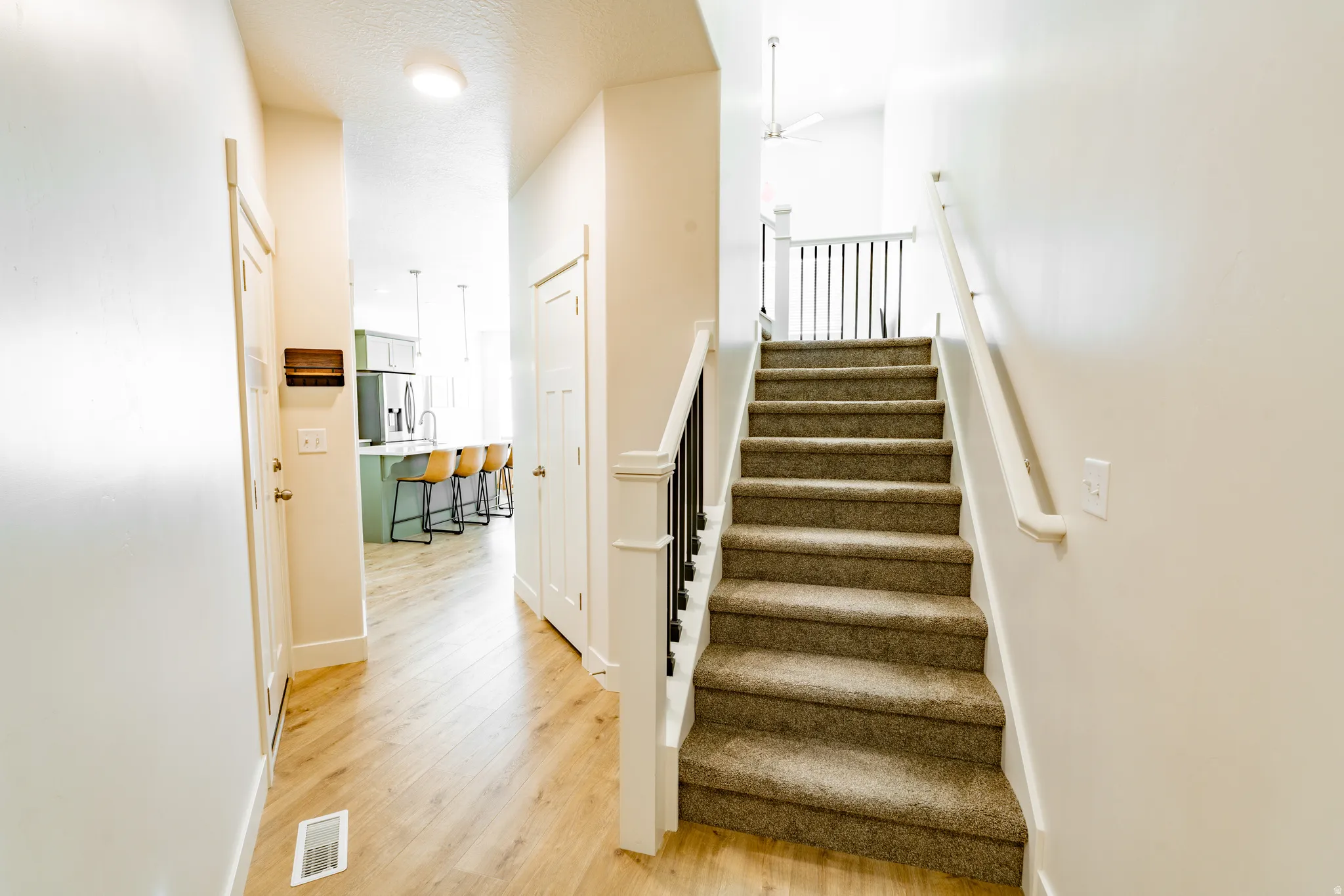 Carpeted staircase with white balusters and dark spindles leading to a landing with a ceiling fan