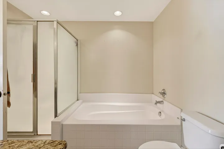 White built-in soaking tub with chrome fixtures, surrounded by white tile and light-toned walls