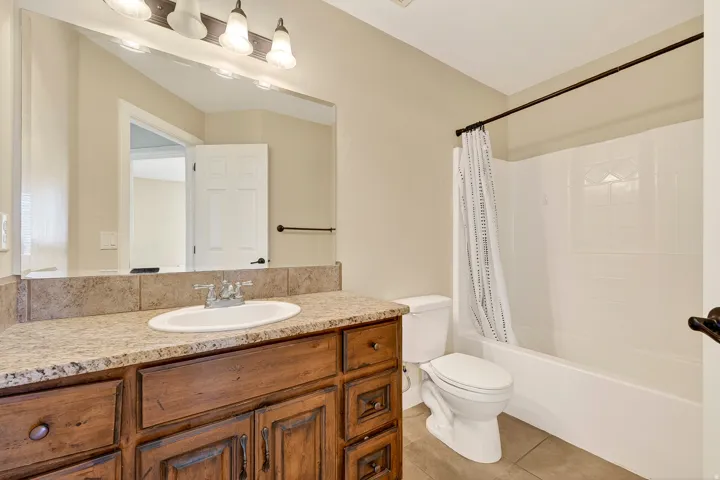 Bathroom featuring a wood-finish vanity with a surface-mount sink, a speckled countertop, and a tiled backsplash