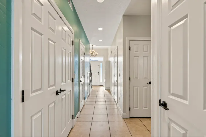 Hallway with tile flooring, recessed lighting, white paneled doors, and a decorative chandelier visible at the far end