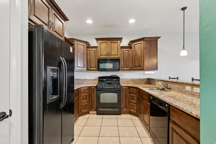 Kitchen featuring wood cabinetry, granite countertops, tile flooring, a built-in microwave, and a black appliance package