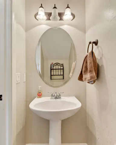 Pedestal sink with chrome-finish faucet, an oval mirror, and a three-light vanity fixture