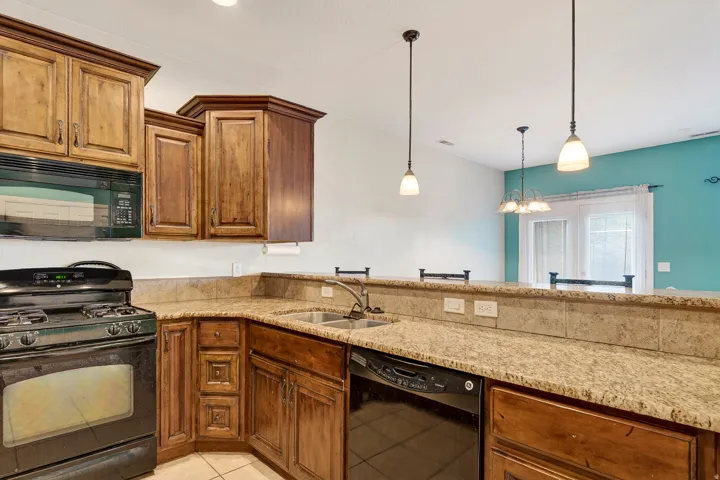 Kitchen featuring wood cabinetry, black appliances including a range and over-the-range microwave, a double basin sink, and a granite-finish countertop with a matching backsplash