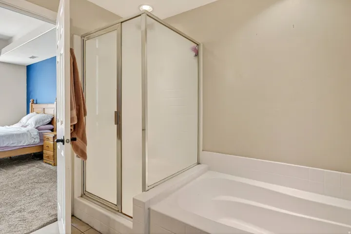 Bathroom featuring an enclosed shower with frosted glass panels and a white built-in bathtub with tiled surround