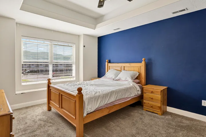 Bedroom featuring a tray ceiling, recessed window with horizontal blinds, and a deep blue accent wall