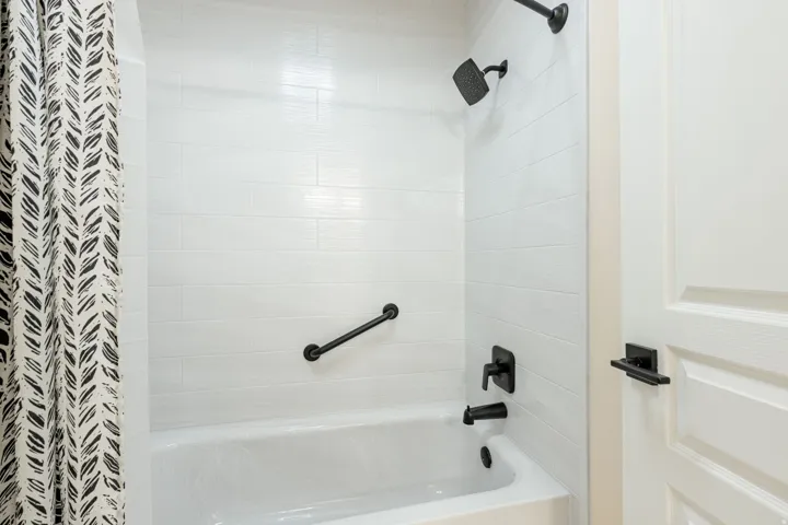 Bathtub with subway tile surround, matte black fixtures, and a coordinating grab bar