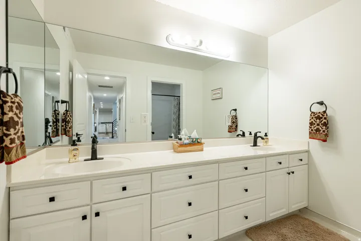 Double vanity with white cabinetry, matte black hardware, and an expansive wall-mounted mirror