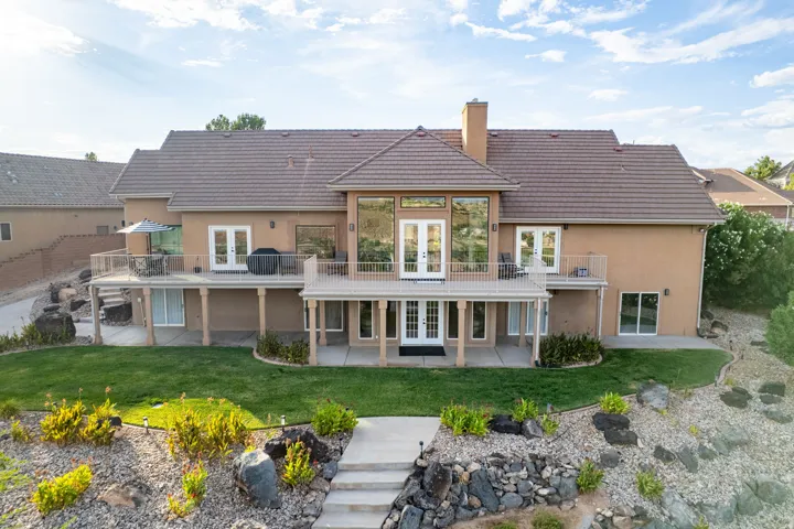 Rear exterior featuring multiple balconies, terraced landscaping, a lower patio, and a manicured lawn
