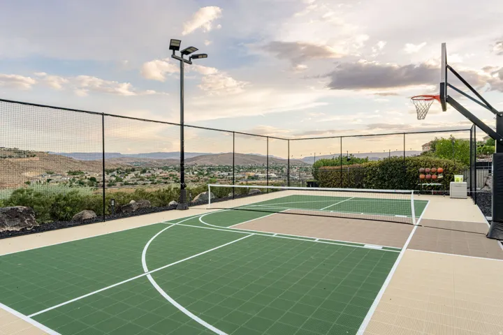 Multi-sport court featuring a basketball hoop and net, surrounded by black chain-link fencing and professional-grade light fixtures