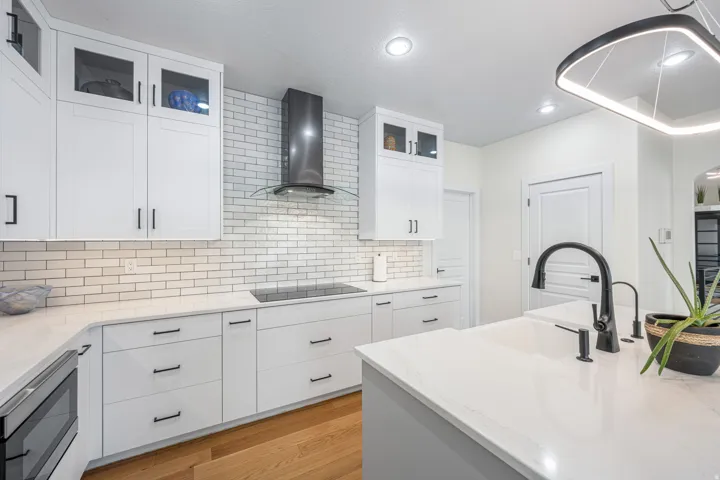 Modern kitchen featuring white shaker cabinetry, an integrated cooktop, subway tile backsplash, quartz countertops, and a contemporary island with a matte black faucet