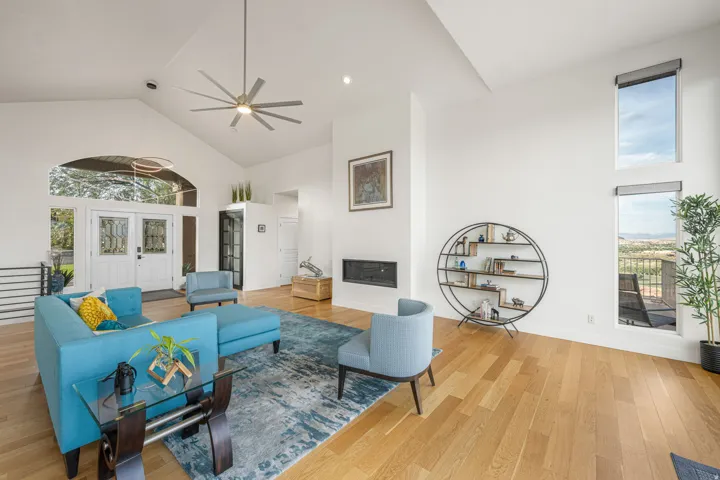 Spacious living area featuring high vaulted ceilings, light wood-finish flooring, a contemporary ceiling fan, a built-in fireplace, and expansive windows