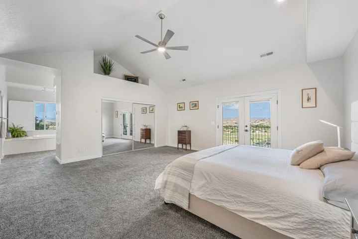 Vaulted ceilings accent a spacious room featuring wall-to-wall carpeting, a built-in jetted tub, a ceiling fan with integrated lighting, and a private balcony with double doors