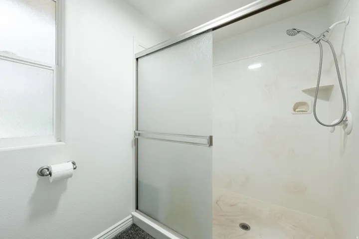 Shower enclosure with a sliding frosted glass door, featuring a handheld showerhead, integrated shelving, and a patterned shower surround