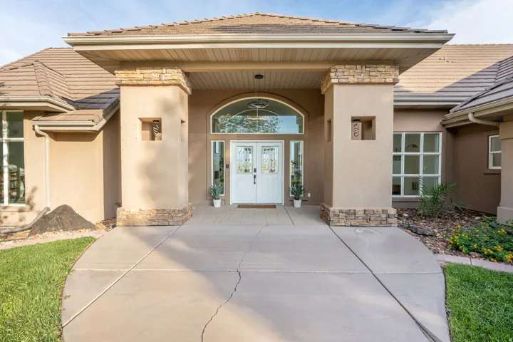 Stucco exterior featuring a covered entry with stone-clad columns, double entry doors with decorative glass panels, and an arched transom window