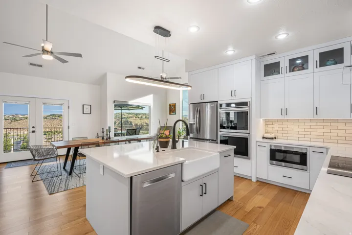 Modern kitchen featuring white shaker cabinetry, stainless steel appliances, a center island with a farmhouse sink, and wood-finish flooring
