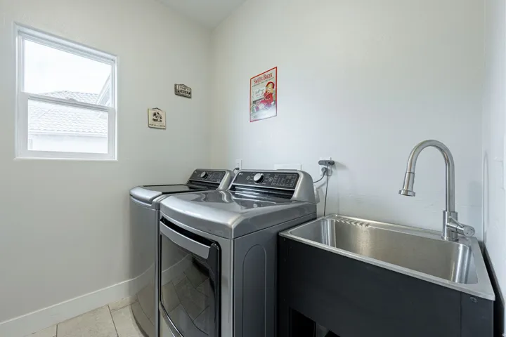 Utility room featuring a window, tile flooring, and a stainless steel sink with a gooseneck faucet
